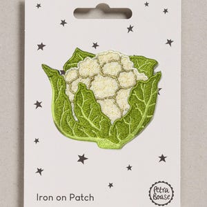 May include: An embroidered iron-on patch shaped like a head of cauliflower with a white floret and green leaves. The patch is attached to a white rectangular display card featuring black star icons, the text "Iron on Patch" and "Petra Boase".