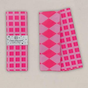 May include: Pink tissue paper with a grid and diamond pattern. The tissue paper is labelled "Luxury Tissue Paper" with a sheet size of 50 x 70cm. The tissue paper is folded and stacked.