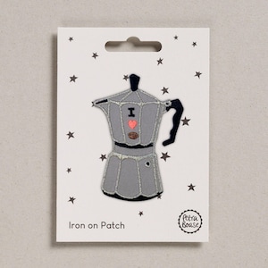 May include: Gray iron-on patch featuring a stylized coffee maker design. The patch includes a pink heart, a coffee bean, and the text "I". The patch is on a white card with black star accents and the text "Iron on Patch".
