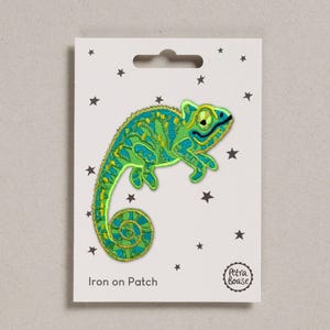 May include: An iron-on patch featuring a detailed embroidered chameleon in shades of green, blue, and yellow. The patch is on a white card with black star accents and the text "Iron on Patch". The Petra Boase logo is in the lower right corner.