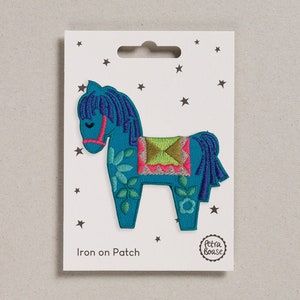 May include: Iron-on patch featuring a blue horse with green, pink, and yellow floral embroidery. The patch is on a white card with stars and the text "Iron on Patch" and "Petra Boase".