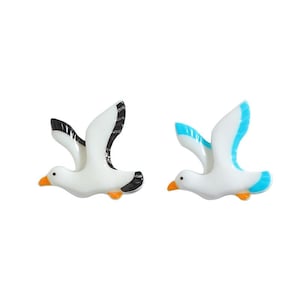 May include: Two ceramic seagull figurines, one with black and white wings and the other with blue and white wings.