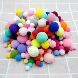 May include: A collection of multi-coloured pom-poms in different sizes and hues, such as pink, blue, yellow, green, orange, and purple. These soft, round craft items are arranged on a pale pink, checkered background.