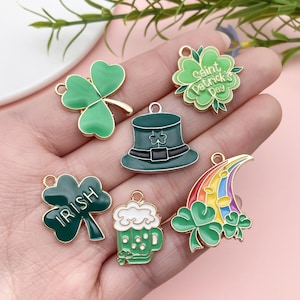 Könnte beinhalten: Sechs goldfarbene Charms mit grünen Emaille-Kleeblättern, einem Regenbogen, einem Bierkrug, einem Leprechaun-Hut und einem Kleeblatt mit dem Text "Saint Patrick's Day".