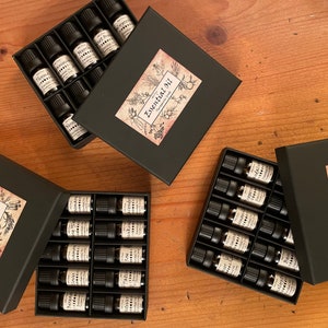 May include: Three black boxes filled with small glass bottles of essential oils. Each box has a label that says "Essential Oil" with a botanical illustration.