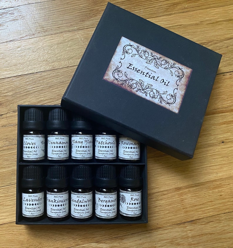 May include: A black box with a label that says "Premium Essential Oil" contains ten small glass bottles of essential oils. The bottles are labeled with the names of the oils, including "Cloves", "Cinnamon", "Ylang Ylang", "Patchouli", "Rosemary", "Lavender", "Frankincense", "Sandalwood", "Bergamot", and "Rose".