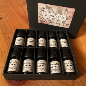 May include: A black box filled with 10 small glass bottles of essential oils. Each bottle has a black cap and a label with the name of the oil, "Essential Oil", and "Therapeutic Grade".