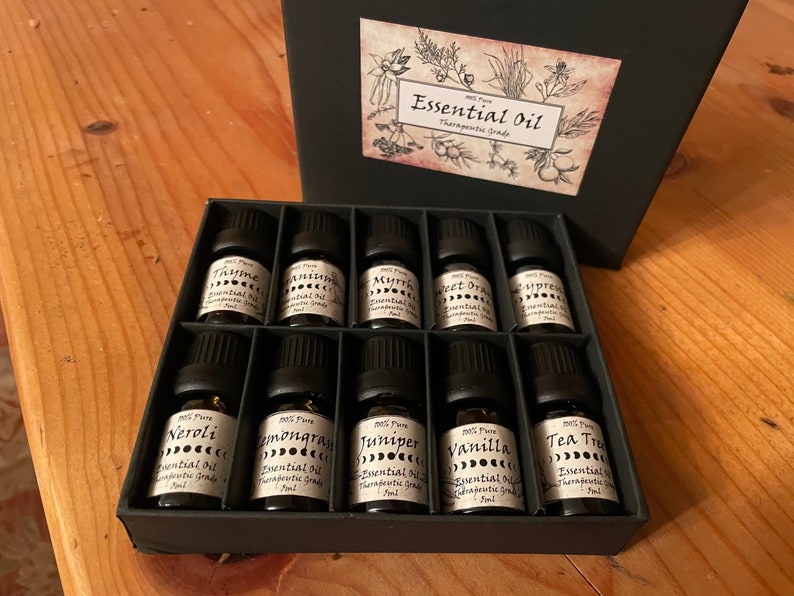 May include: A black box filled with 10 small glass bottles of essential oils. Each bottle has a black cap and a label with the name of the oil, "Essential Oil", and "Therapeutic Grade".