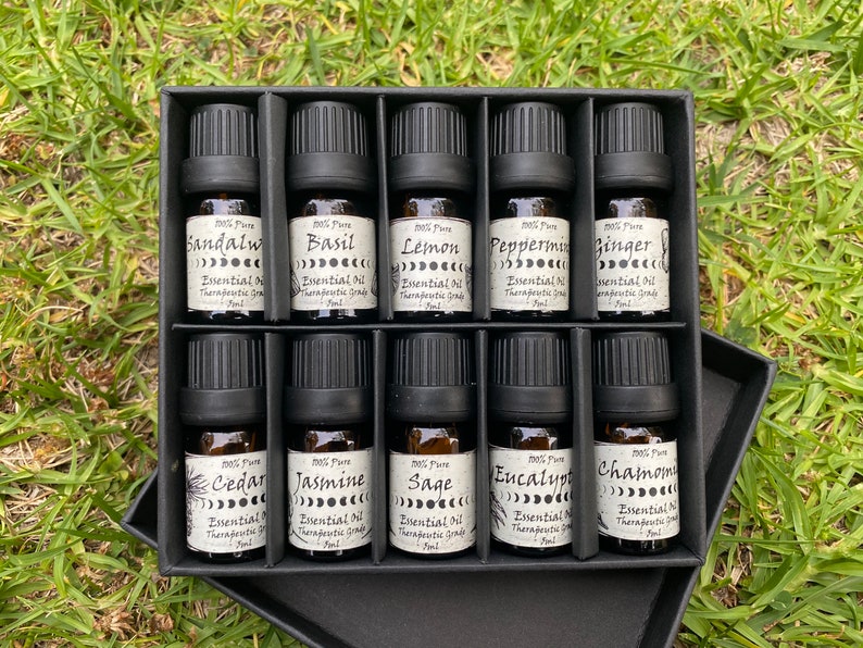 May include: A black box with 10 small glass bottles containing essential oils. The bottles are labeled with the names of the oils, including Sandalwood, Basil, Lemon, Peppermint, Ginger, Cedar, Jasmine, Sage, Eucalyptus, and Chamomile.