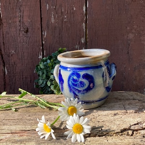 Peut inclure: Un pot en céramique bleu et blanc avec un motif floral posé sur une surface en bois vieilli avec trois marguerites blanches.
