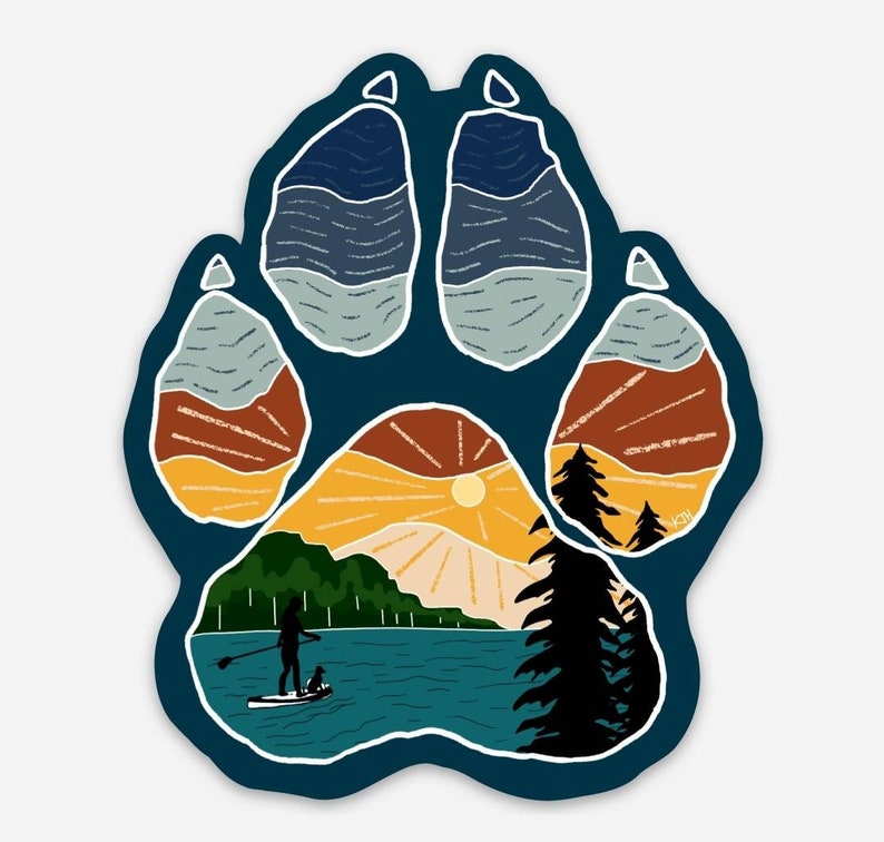 Puede incluir: Una huella de pata azul con una escena de puesta de sol en su interior. La escena incluye un lago, monta&ntilde;as, &aacute;rboles y una persona haciendo paddleboard con un perro.