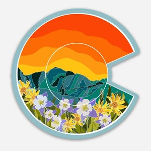 Puede incluir: Una pegatina colorida que presenta un contorno estilizado del estado de Colorado. La pegatina representa una cordillera con un cielo de puesta de sol y un campo de flores silvestres en primer plano.