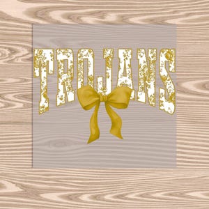 May include: A graphic design featuring the word "TROJANS" in a gold floral pattern, with a gold bow at the center. The design is set against a light gray background, placed on a wooden surface.