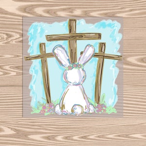 May include: A white bunny with a flower crown sits in front of three wooden crosses against a blue and white background.