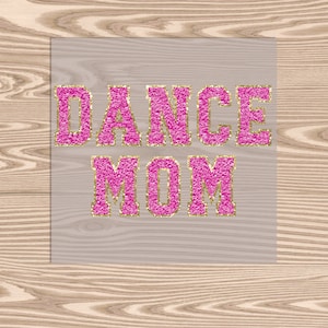 May include: A pink and gold glitter sign with the text "DANCE MOM" on a light brown woodgrain background.