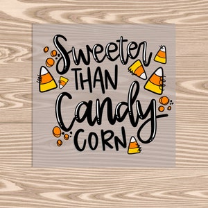 May include: A sign with the text "Sweeter than Candy Corn" in black script font. The sign is decorated with orange, yellow, and white candy corn illustrations.