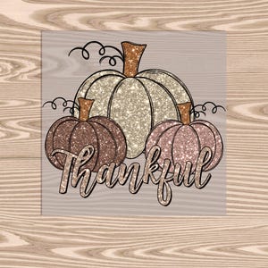 May include: A digital illustration of three pumpkins with glitter textures. The pumpkins are in shades of gold, brown, and pink. The text "Thankful" is written in a decorative font below the pumpkins.