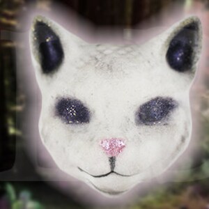May include: White ceramic cat head with black eyes and a pink nose. The cat's eyes have a sparkly texture.