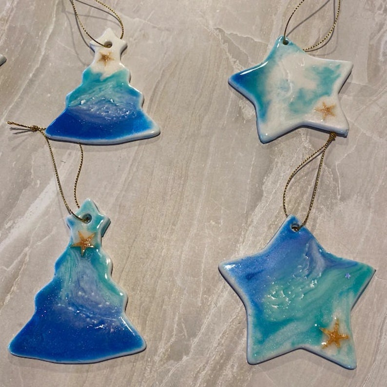 Puede incluir: Cinco adornos navide&ntilde;os hechos a mano, dos son adornos de &aacute;rbol azul y blanco y tres son adornos de estrella azul y blanco. Cada adorno tiene una estrella dorada.