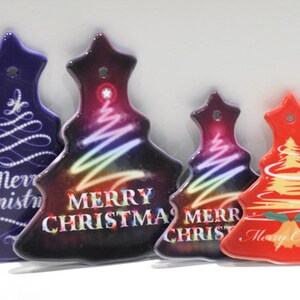 Puede incluir: Cuatro adornos de &aacute;rbol de Navidad de cer&aacute;mica con diferentes dise&ntilde;os. Los adornos son de color morado, negro, rojo y blanco con las palabras "Feliz Navidad" en cada uno.
