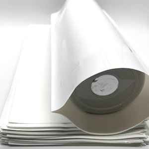 May include: A roll of white vinyl sticker paper, with a stack of sheets underneath. The paper is rolled up and secured with a white label.