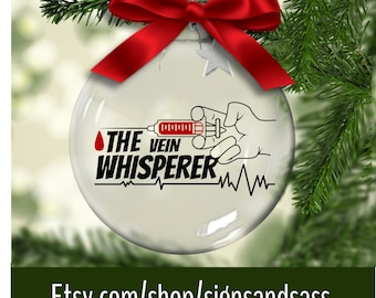May include: Clear glass Christmas ornament with a red ribbon and green pine branches. The ornament features the text "THE VEIN WHISPERER" with a syringe graphic and a heartbeat line. The Etsy shop URL is visible at the bottom.