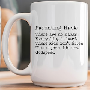 May include: White ceramic mug with a black text that reads "Parenting Hack: There are no hacks. Everything is hard. These kids don't listen. This is your life now. Godspeed."