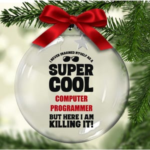 May include: A clear glass Christmas ornament with the text "I NEVER IMAGINED MYSELF AS A SUPER COOL COMPUTER PROGRAMMER BUT HERE I AM KILLING IT!". The ornament has a red bow and is hanging on a Christmas tree.