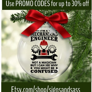 May include: Clear glass Christmas ornament with the text "I'M A MECHANICAL ENGINEER" and a graphic of a person in a hard hat holding a wrench. The ornament is decorated with a red bow and set against a backdrop of pine needles.