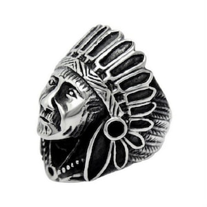 May include: A silver-colored ring featuring a detailed depiction of a Native American chief wearing a feathered headdress. The ring has a textured, oxidized finish, and the design is highly detailed.