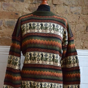 以下が含まれることがあります： クリーム、緑、茶色、黒のラマと木の繰り返し模様が特徴の、ハイネックの柄入りセーター。セーターは緑色のベースにオレンジと黒のバンドが付いています。袖口と袖口は緑色です。