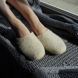 May include: A pair of off-white wool slippers on a gray knitted blanket.