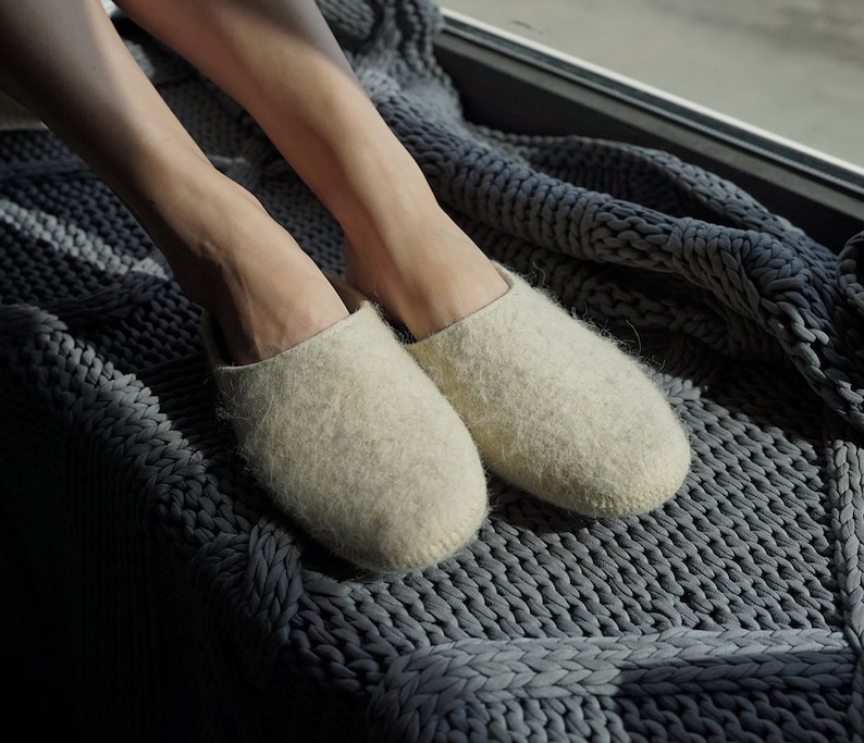 May include: A pair of off-white wool slippers on a gray knitted blanket.