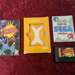 May include: A collection of Sega 32X video game items, including a game cartridge, game box, and a catalog. The game box features the title "Shadow Squadron" with a colorful graphic. The catalog features Sonic the Hedgehog and Knuckles.