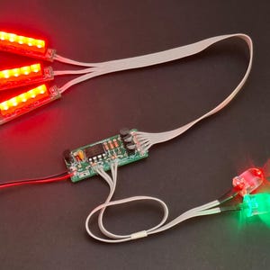 Op de afbeelding: Elektronische componenten met rode en groene LED-verlichting. De afbeelding toont een printplaat met meerdere LED-lampjes, waaronder drie rode LED-strips en twee afzonderlijke rode en groene LED's. De componenten zijn verbonden door witte en zwarte draden.