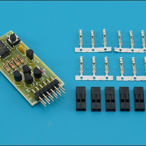 Peut inclure: Une carte de circuit imprimé verte avec un bouton, des résistances et une puce. La carte a une rangée de broches sur le côté droit. Il y a également 12 blocs de connecteurs noirs et 6 blocs de connecteurs argentés.