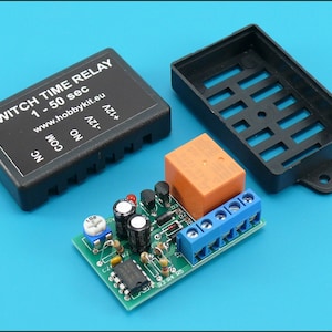 May include: A black plastic case with a green circuit board inside. The circuit board has a small orange relay, a potentiometer, and a few capacitors. The case has a label that reads "SWITCH TIME RELAY 1-50 sec www.hobbykit.eu NC COM ON  12V+  AC1+"