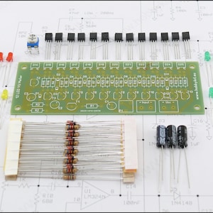 May include: An electronic DIY kit featuring a green rectangular printed circuit board labelled 12 LED VU Meter, accompanied by various components including resistors, capacitors, transistors, a potentiometer, and yellow and green LEDs.