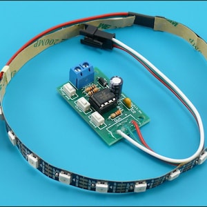 Peut inclure: Un contrôleur de circuit imprimé électronique vert doté d'un bornier bleu, d'une puce de circuit intégré noire et de trois boutons-poussoirs blancs, relié à une bande lumineuse LED flexible avec support adhésif et connecteurs noirs.