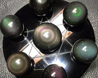 May include: Seven iridescent black obsidian spheres with swirling patterns of green, blue, and purple are arranged on a black circular base.
