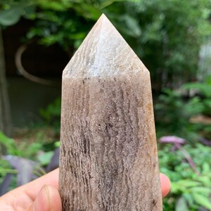 May include: A light brown and gray crystal point with a pointed top and a textured surface.