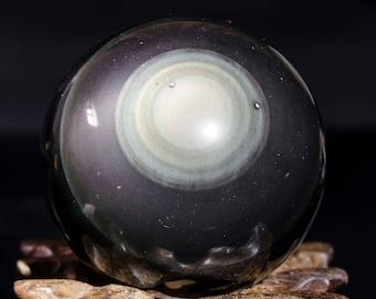 May include: A black obsidian sphere with a swirling, iridescent pattern in the center. The sphere is sitting on a wooden stand.