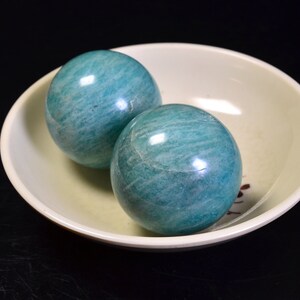 May include: Two smooth, green, round, polished, gemstone spheres in a white bowl. The spheres are made of amazonite.