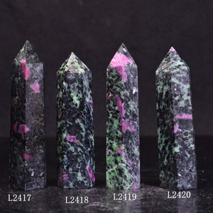 Może przedstawiać: Cztery polerowane obeliski z kamieni szlachetnych. Każdy obelisk ma ciemny, nakrapiany kolor z zielonymi i różowymi wtrąceniami. Obeliski są oznaczone jako L2417, L2418, L2419 i L2420.