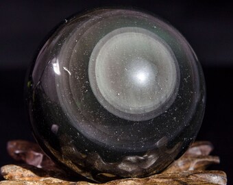 May include: A black obsidian sphere with a swirling, concentric pattern. The sphere is resting on a wooden stand.