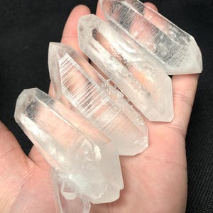 May include: Four clear quartz crystal points, also known as rock crystals, with a natural, raw finish. The points are arranged in a stack, with the tips of the points facing upwards. The crystals are translucent and have a slight shimmer.