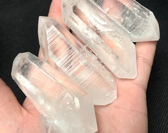May include: Four clear quartz crystal points, also known as rock crystals, with a natural, raw finish. The points are arranged in a stack, with the tips of the points facing upwards. The crystals are translucent and have a slight shimmer.