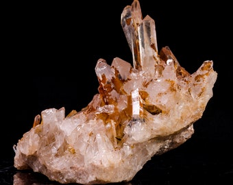 May include: A cluster of clear quartz crystals with a reddish-brown hue, forming a unique and intricate shape. The crystals are set against a black background, highlighting their natural beauty.