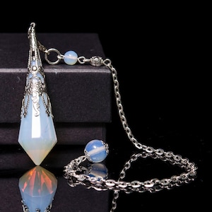 May include: A silver and opal pendulum with a chain and a small opal bead. The pendulum is on a black surface.