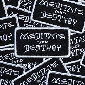 May include: A close-up of several black fabric patches with white embroidered text that reads "Meditate and Destroy".